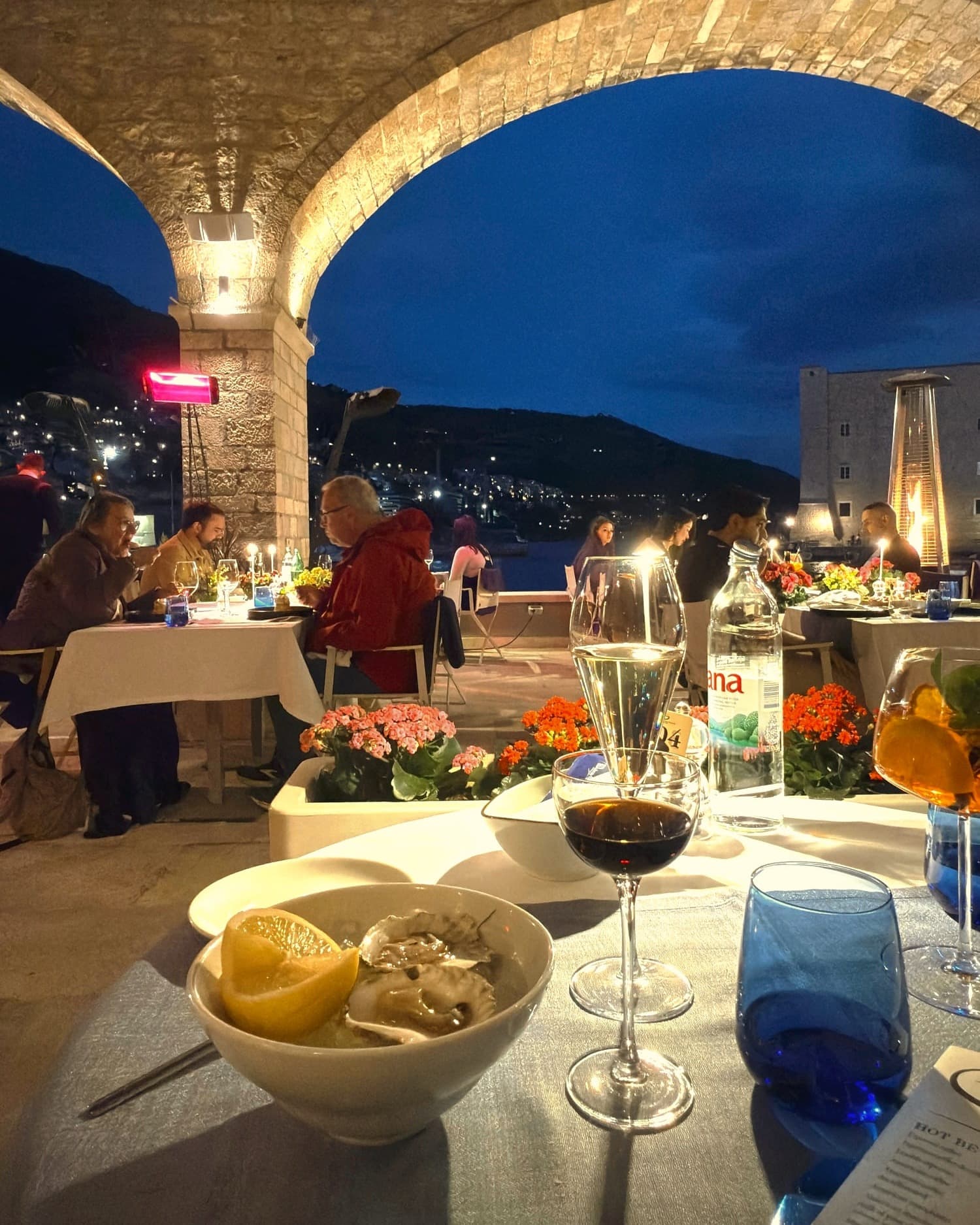 Oysters and wine on a terrace table in Dubrovnik at dusk, with the old town behind