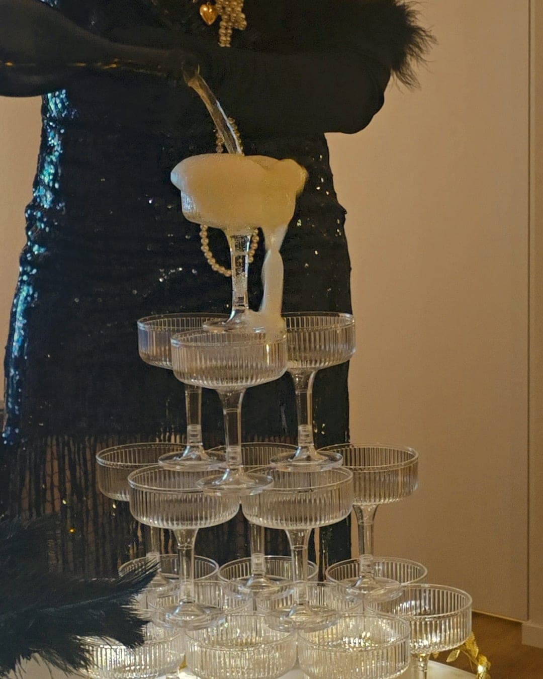 Champagne pouring down a tower of coupe glasses wrapped in gold garland