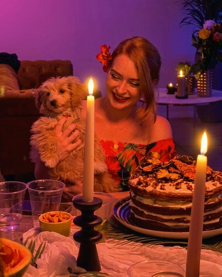 Eva laughing by candlelight with Coco in her arms, beside the layered birthday cake
