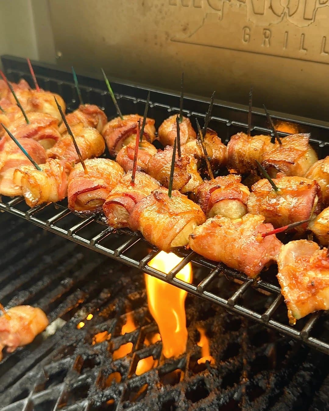 Bacon-wrapped banana bites on toothpicks, crisping on a grill rack over an open flame