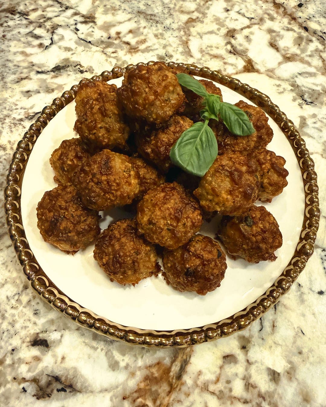Baked Italian turkey meatballs piled on a gold-rimmed plate, topped with basil