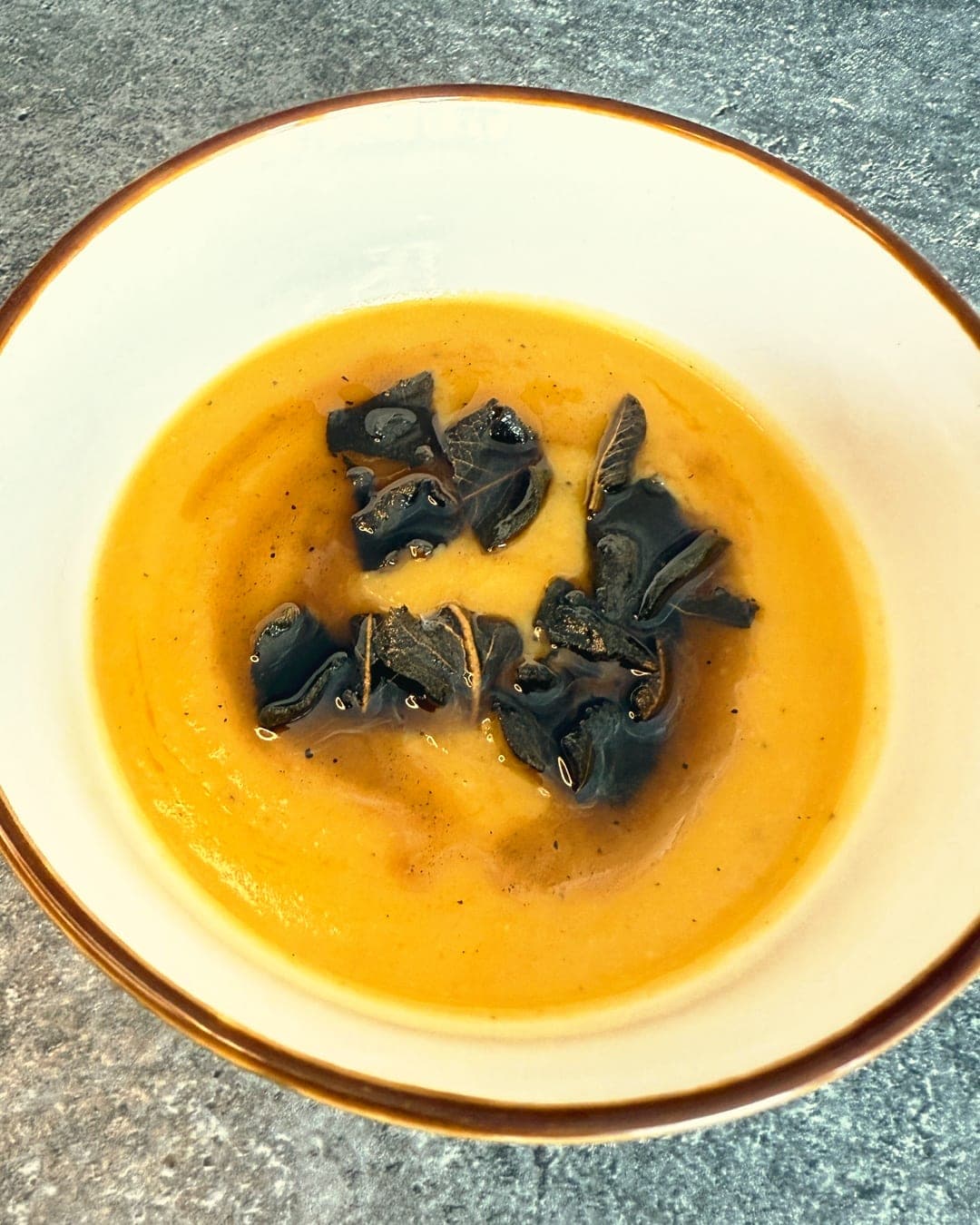 A bowl of smooth roasted butternut squash soup topped with crisp fried sage leaves